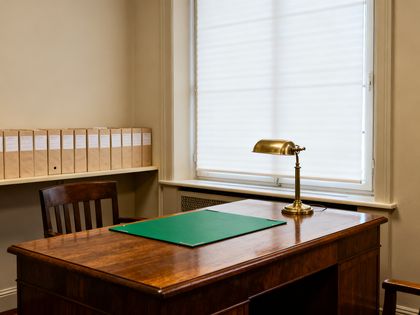 Notarbüro mit schwerem Schreibtisch, Leselampe und einer Reihe gleicher Ordner